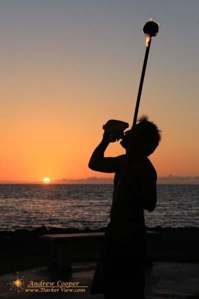 A runner blowing a shell and lighting the torches across the grounds of the Fairmont Orchid at sunset