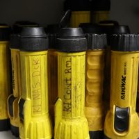 A collection of well used spare flashlights sitting on a shelf