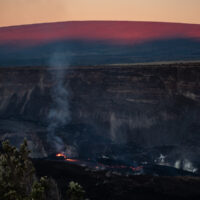 The active vent erupts lava as the dawn illuminates Mauna Loa behind